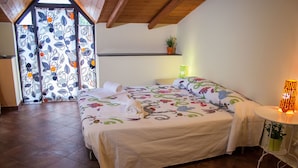 A bedroom with a large bed, a small bedside table, a potted plant, and a window with patterned curtains. - Le Coccole (Catania)