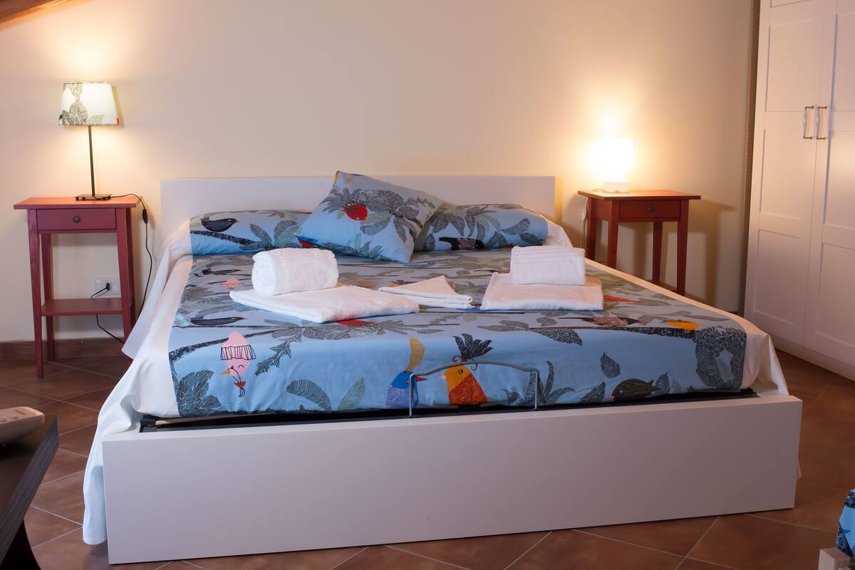 Un lit bien fait, avec une literie à motifs floraux, deux tables de chevet avec des lampes et une armoire en arrière-plan.