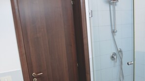 A bathroom with a wooden door, a glass shower enclosure, and a white sink. - Le Coccole (Catania)