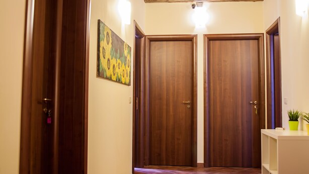 A hallway with two wooden doors, a painting on the wall, and a small shelf with plants. - Le Coccole (Catania)