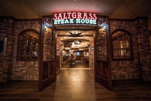 The entrance to a steak house with a brick facade and a neon sign.
