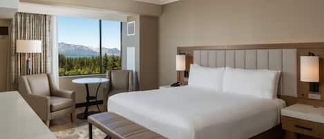 A hotel room with a large bed, a desk, a chair, a small table, and a view of mountains.