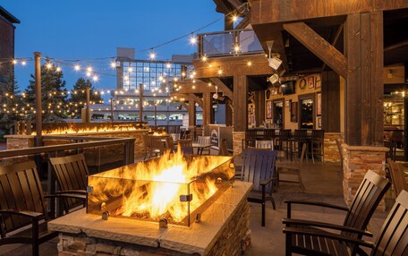 An outdoor seating area with a fire feature, wooden chairs, and string lights.