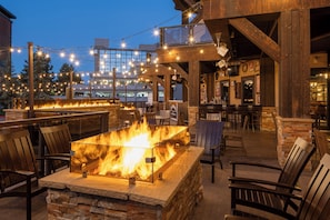 Un espacio al aire libre con asientos, una chimenea, sillas de madera y luces colgantes.