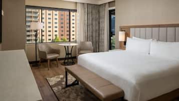 A hotel room with a large bed, a desk, two chairs, a small table, and a bench.