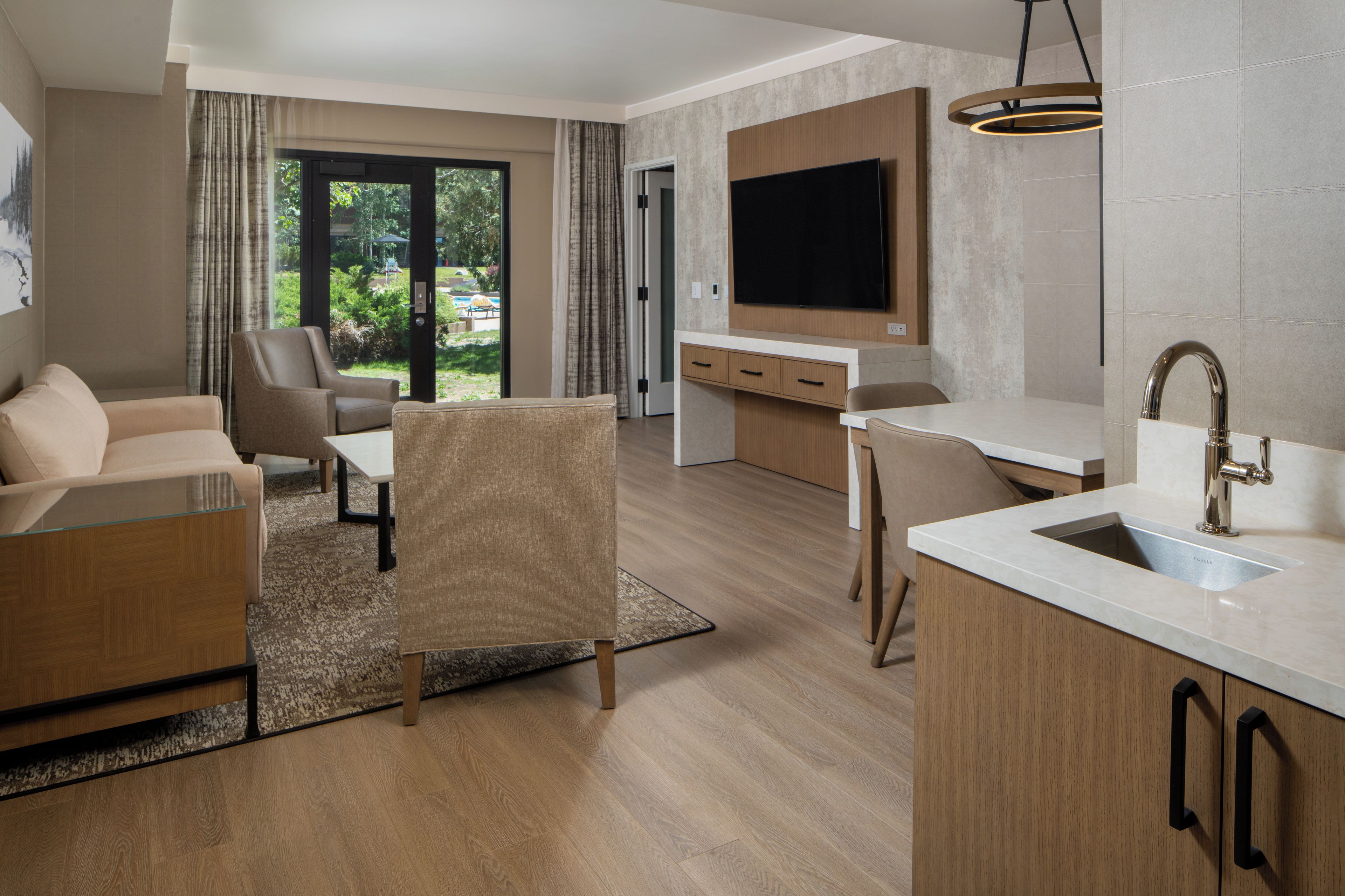 Una sala de estar moderna con un sofá, una silla y una mesa de centro. Cuenta con una zona de cocina con un lavamanos y un televisor.