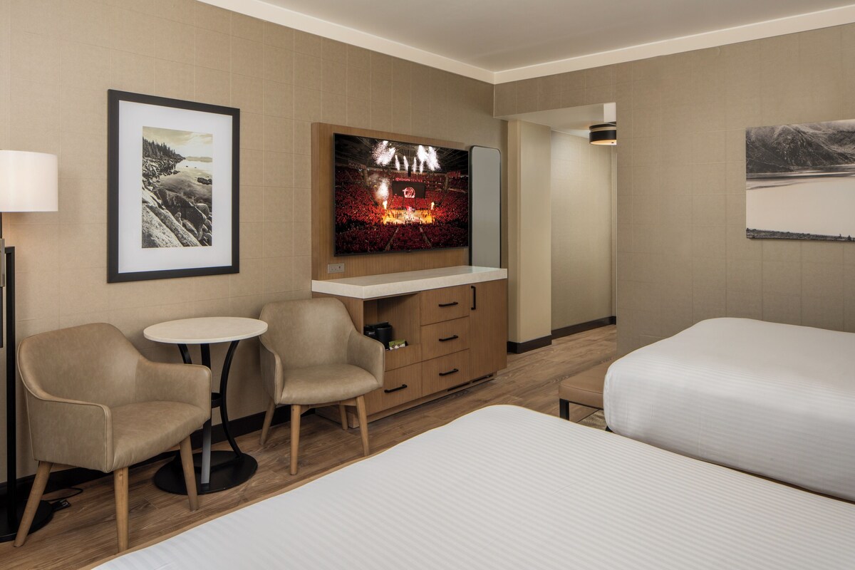 A hotel room with a bed, two armchairs, a small table, a TV, and a dresser.