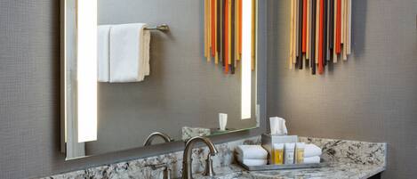 Un baño moderno con lavamanos de mármol, un espejo grande y un perchero con varias toallas.