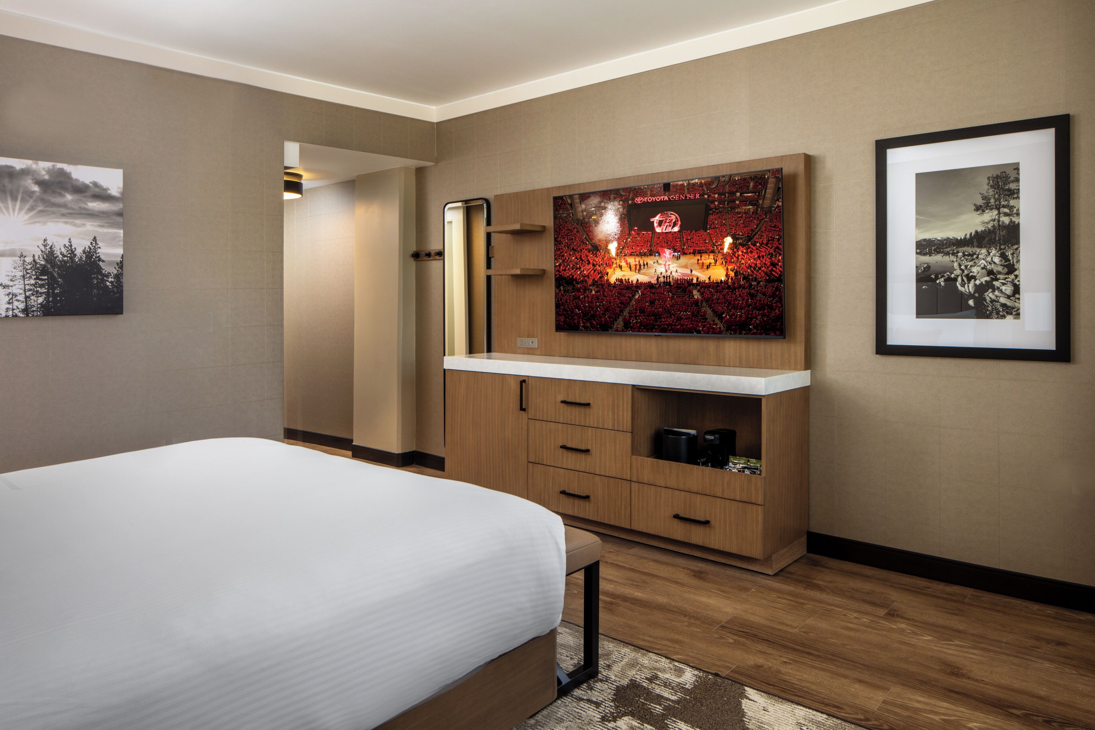 A modern hotel room with a bed, a TV mounted on the wall, wooden cabinets, and a framed picture.