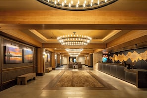 A hotel lobby with a central chandelier, artwork on the walls, a reception desk, and a seating area.