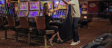 A casino with slot machines, a woman playing a game, and a man standing beside her.