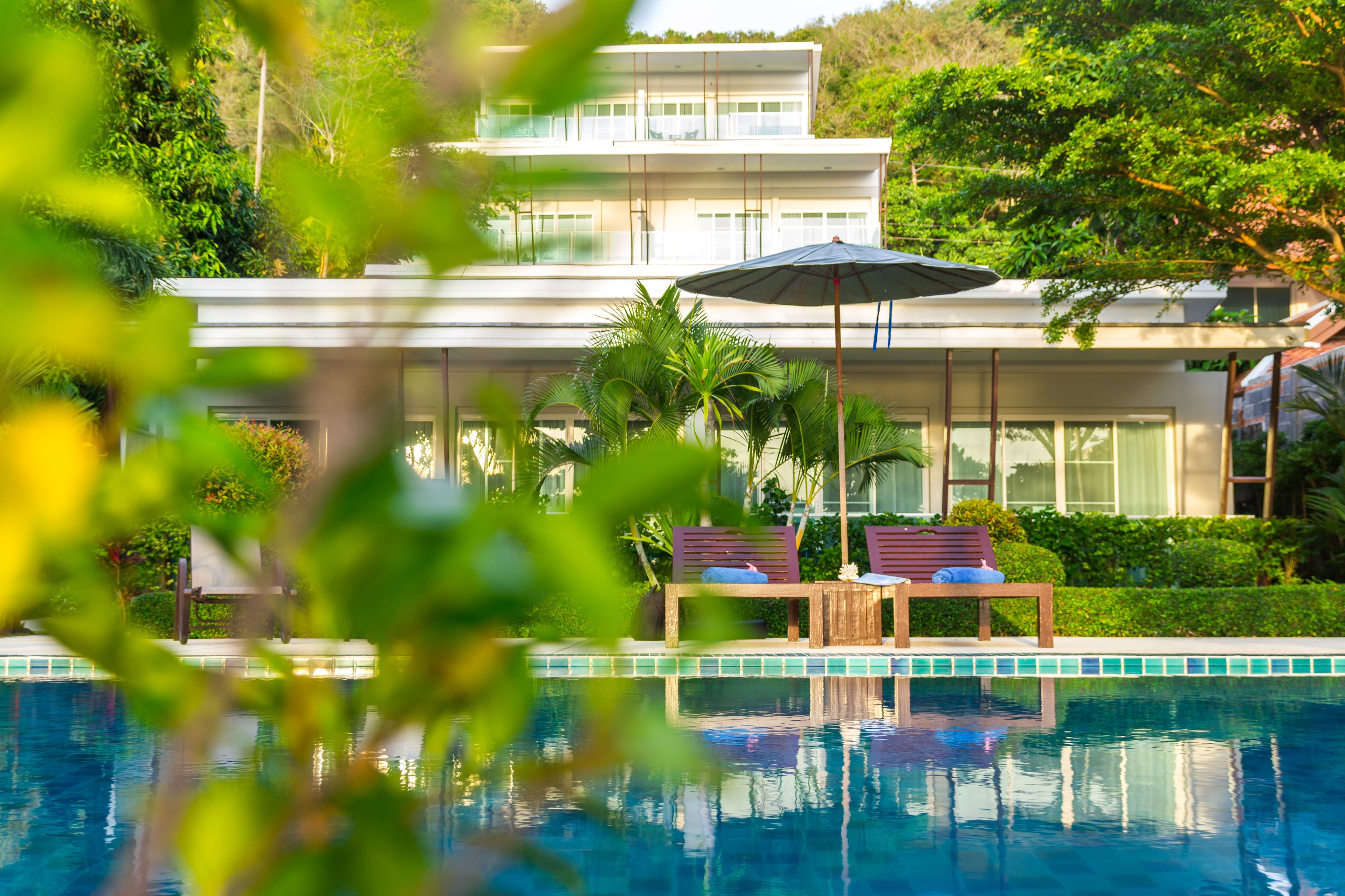 A modern house with a pool, two wooden chairs, and a large umbrella.