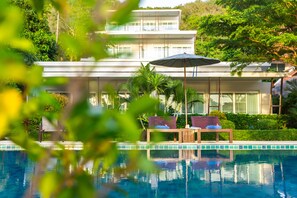 A modern house with a pool, two wooden chairs, and a large umbrella. - Davina Beach Homes (Wichit)
