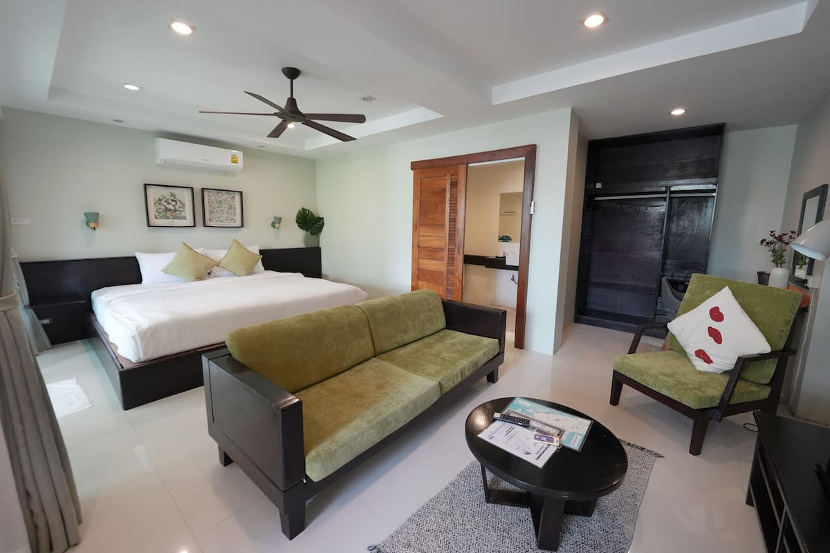 A modern hotel room with a bed, sofa, armchair, and a coffee table.