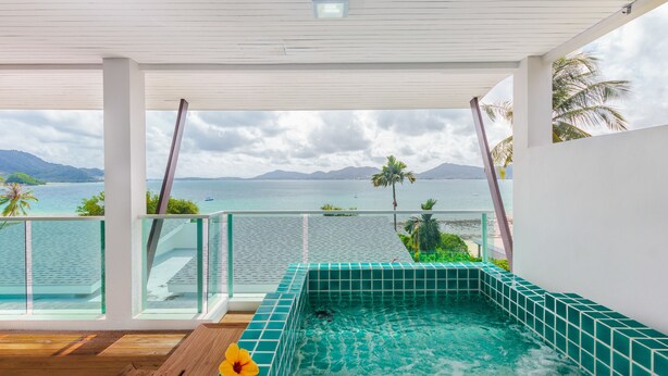 En modern infinitypool med kristallklart blått vatten, ett trädäck och en fantastisk utsikt över havet och bergen.