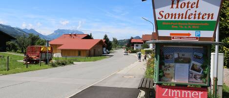 A sign for Hotel Sonnenleiten with a clear view of the surrounding area, including a road, buildings, and mountains in the background.