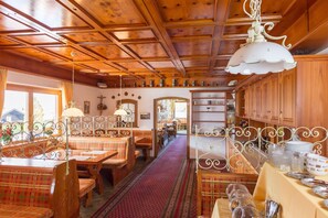 Un restaurante acogedor con interiores de madera, un área central de comedor con bancos y mesas, y una cocina visible al fondo.