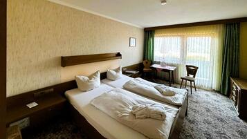 Ein Hotelzimmer mit zwei Betten, einem Schreibtisch, einem Stuhl und einem fenster mit Vorhängen.