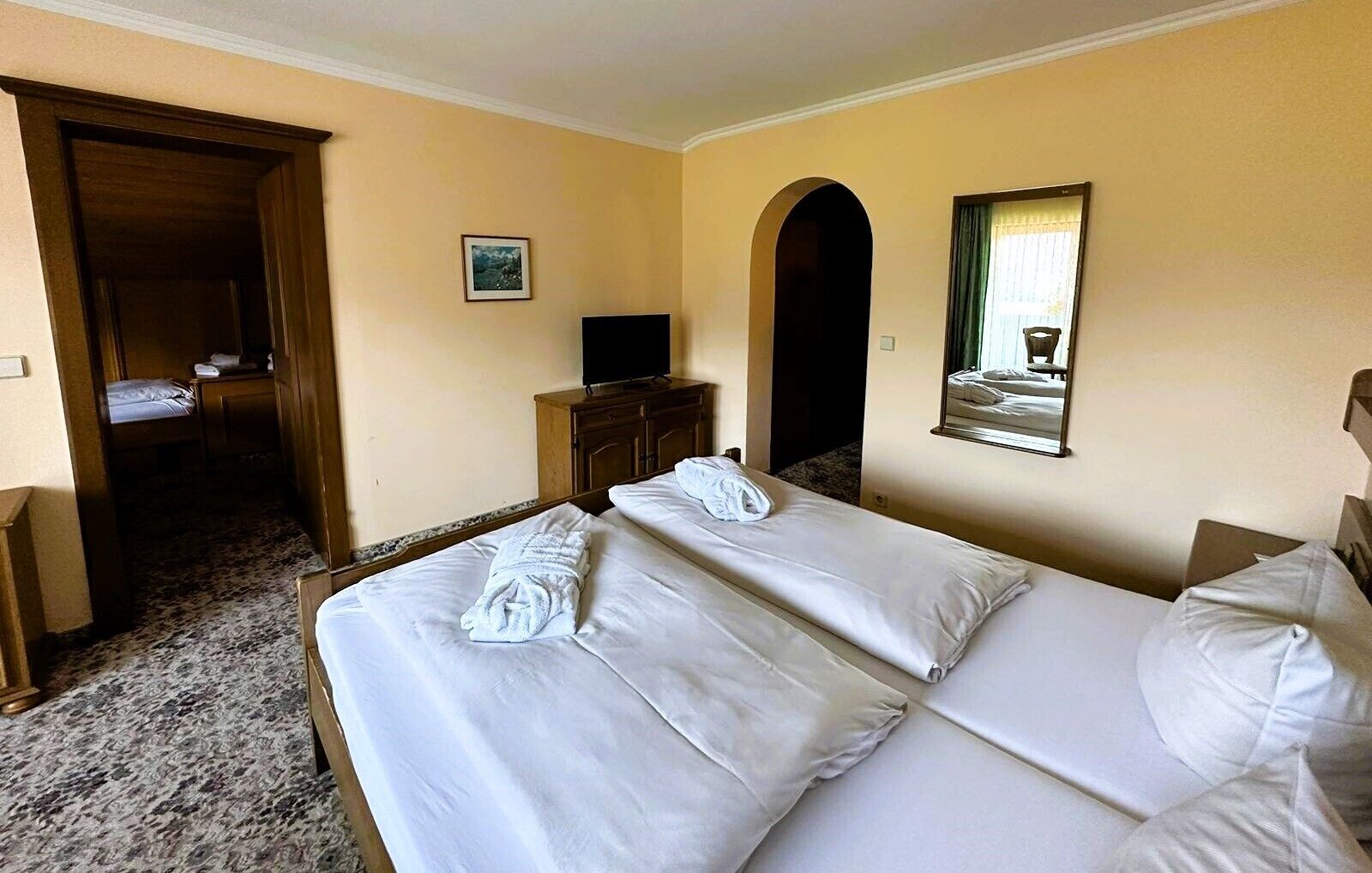 Et hotelværelse med en dobbeltseng, fjernsyn, et spejl og en dør til et badeværelse.