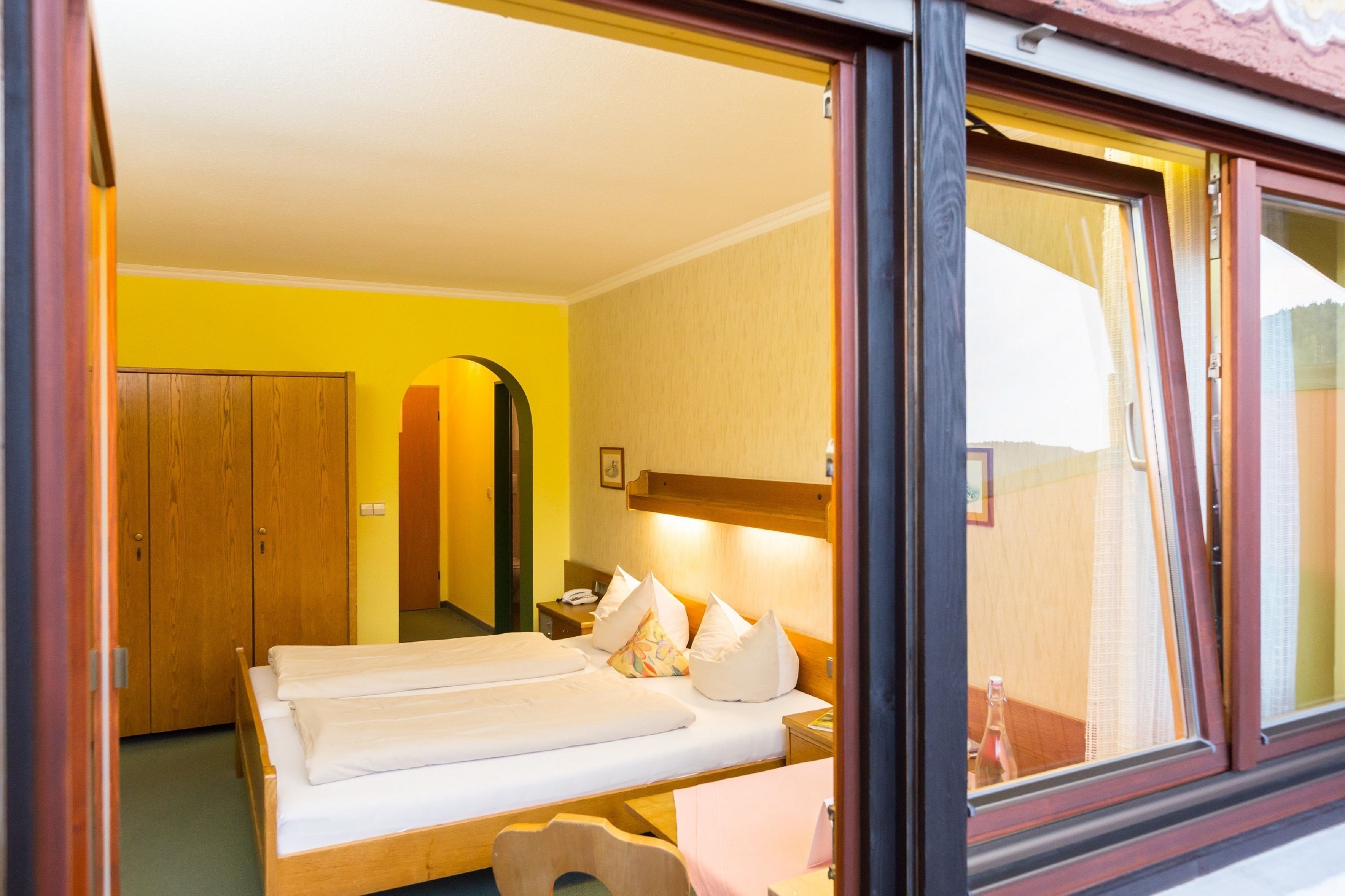 A room with two beds, wooden furniture, a mirror, and a window with curtains.