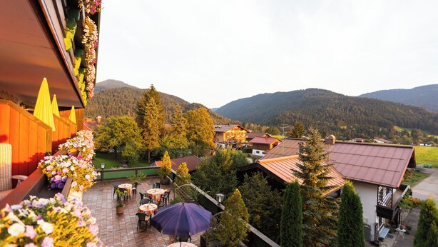 A terrace with outdoor seating, surrounded by flowers and trees, overlooking a mountainous landscape. -  Hotel Sonnleiten (Reit im Winkl)