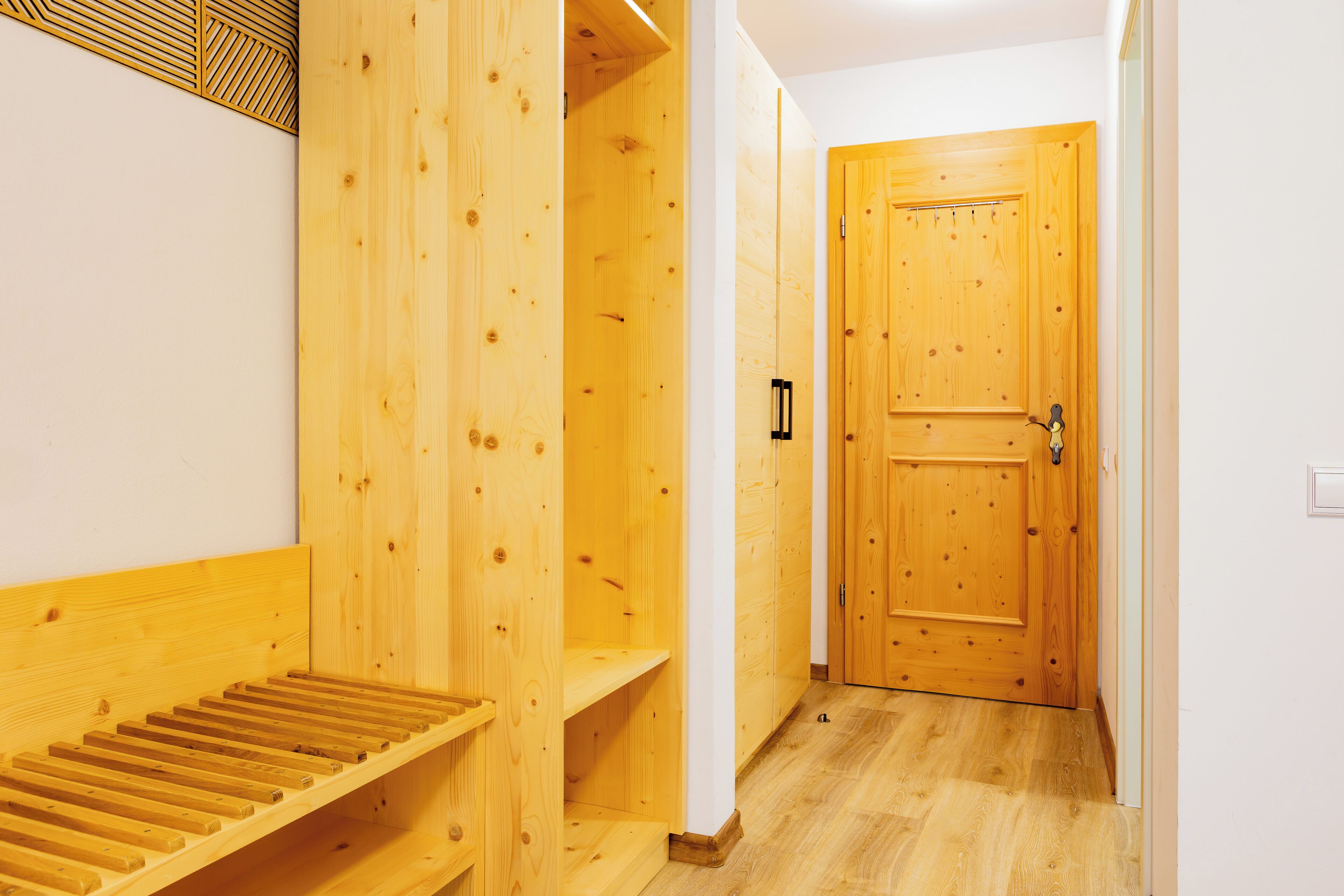Interior de madera con un banco, una puerta y un muro con un diseño geométrico.