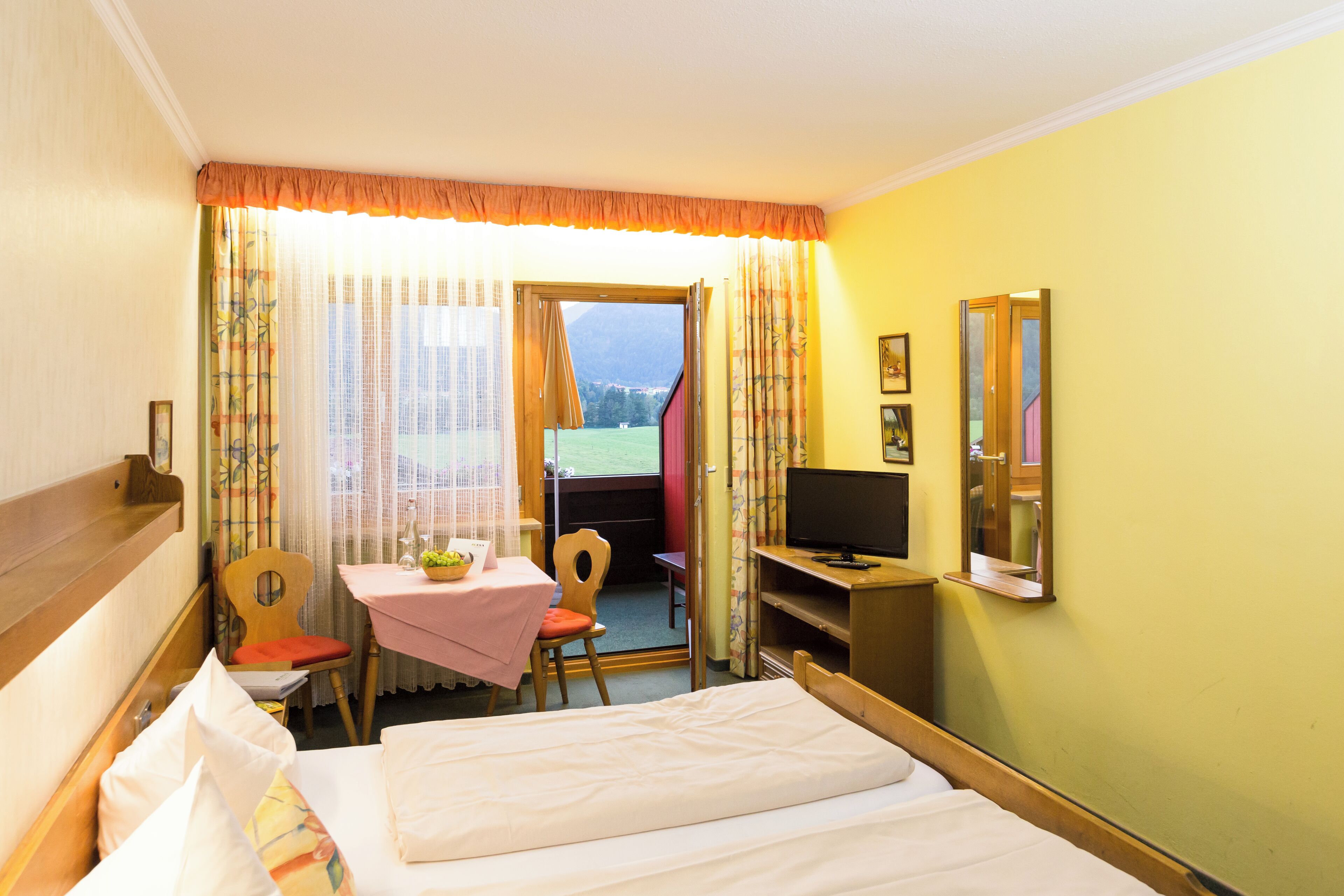 A hotel room with a bed, a desk with a chair, a television, and a window with curtains.