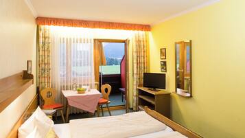 A hotel room with a bed, a desk with a chair, a television, and a window with curtains.
