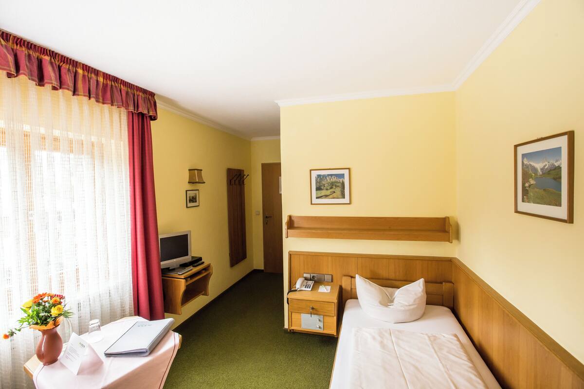 Ein Hotelzimmer mit zwei Betten, einem Schreibtisch mit Computer, einem Nachttisch mit Telefon und einem Fenster mit Vorhängen.