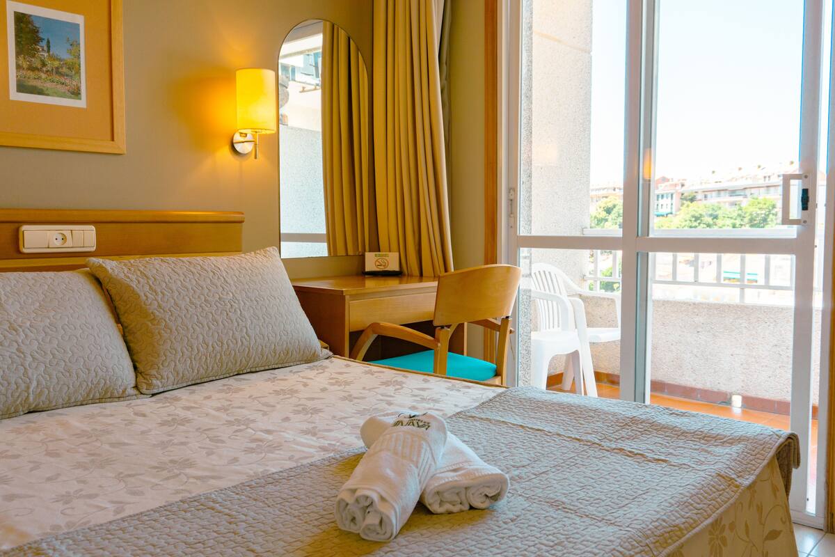 A hotel room with a bed, a desk, a chair, and a view of the outside.