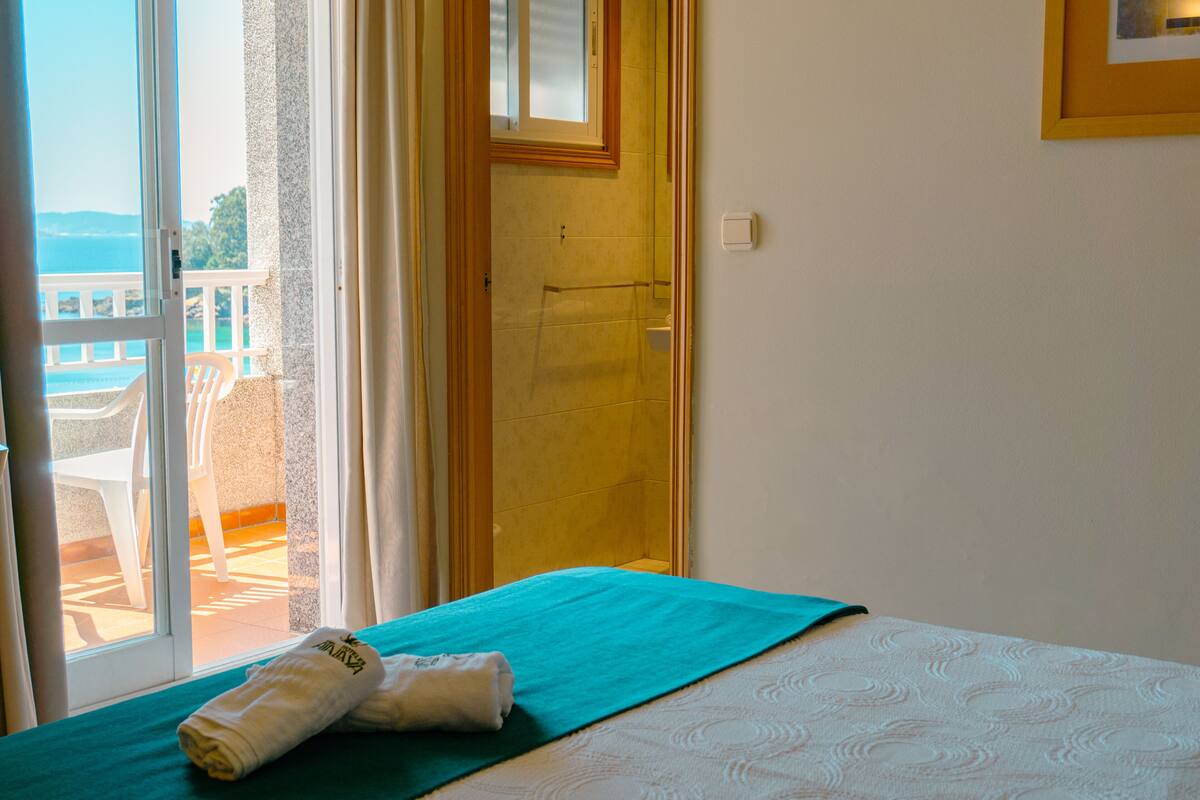 A hotel room with a bed, a window with a view of the sea, and a bathroom with a shower.
