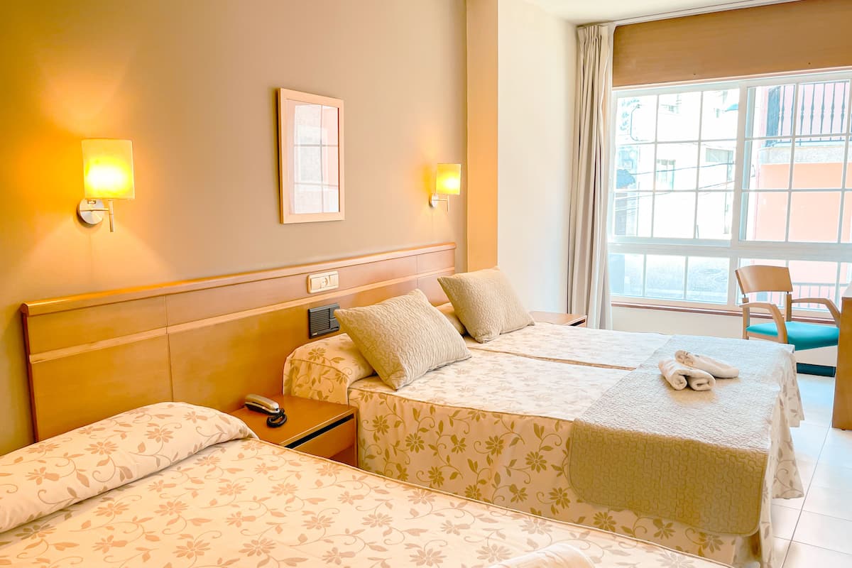 A hotel room with two beds, a nightstand, a chair, and a window with curtains.