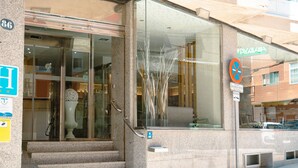 Ein Hotel mit Glasfassade, Stufen zum Eingang und einem Verbotsschild für parkende Fahrzeuge.