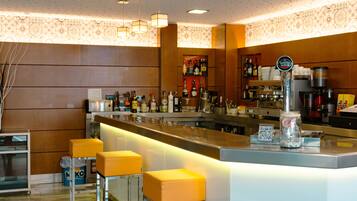 Zona de bar con mostrador, taburetes y una variedad de botellas y vasos.