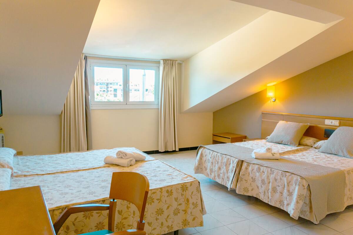 A hotel room with two beds, a desk, a chair, and a window with curtains.