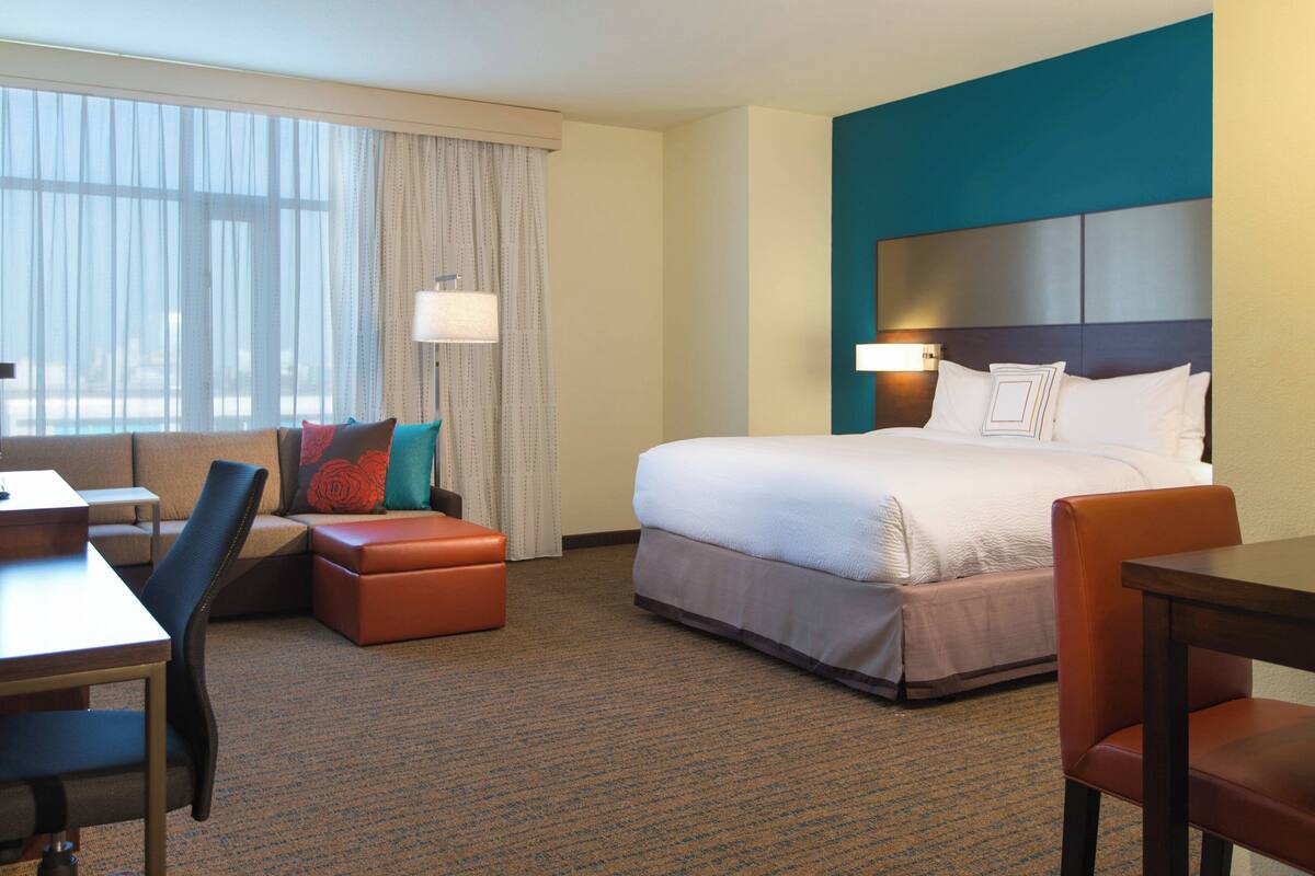 Une chambre d’hôtel avec un lit, un bureau, une chaise, un canapé et une fenêtre avec des rideaux.