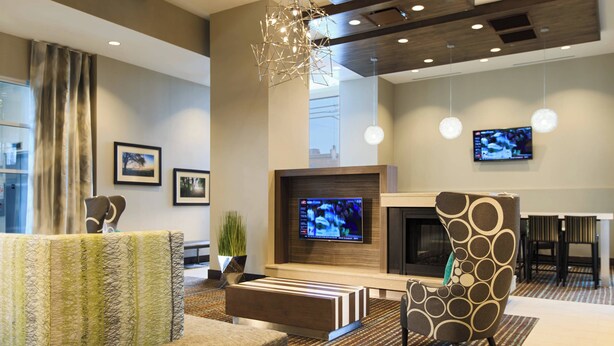 A modern hotel lobby with a sofa, a coffee table, a patterned armchair, a TV, and a fireplace.