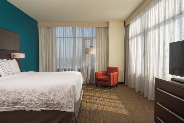 A hotel room with a large bed, a chair, a TV, and a desk.