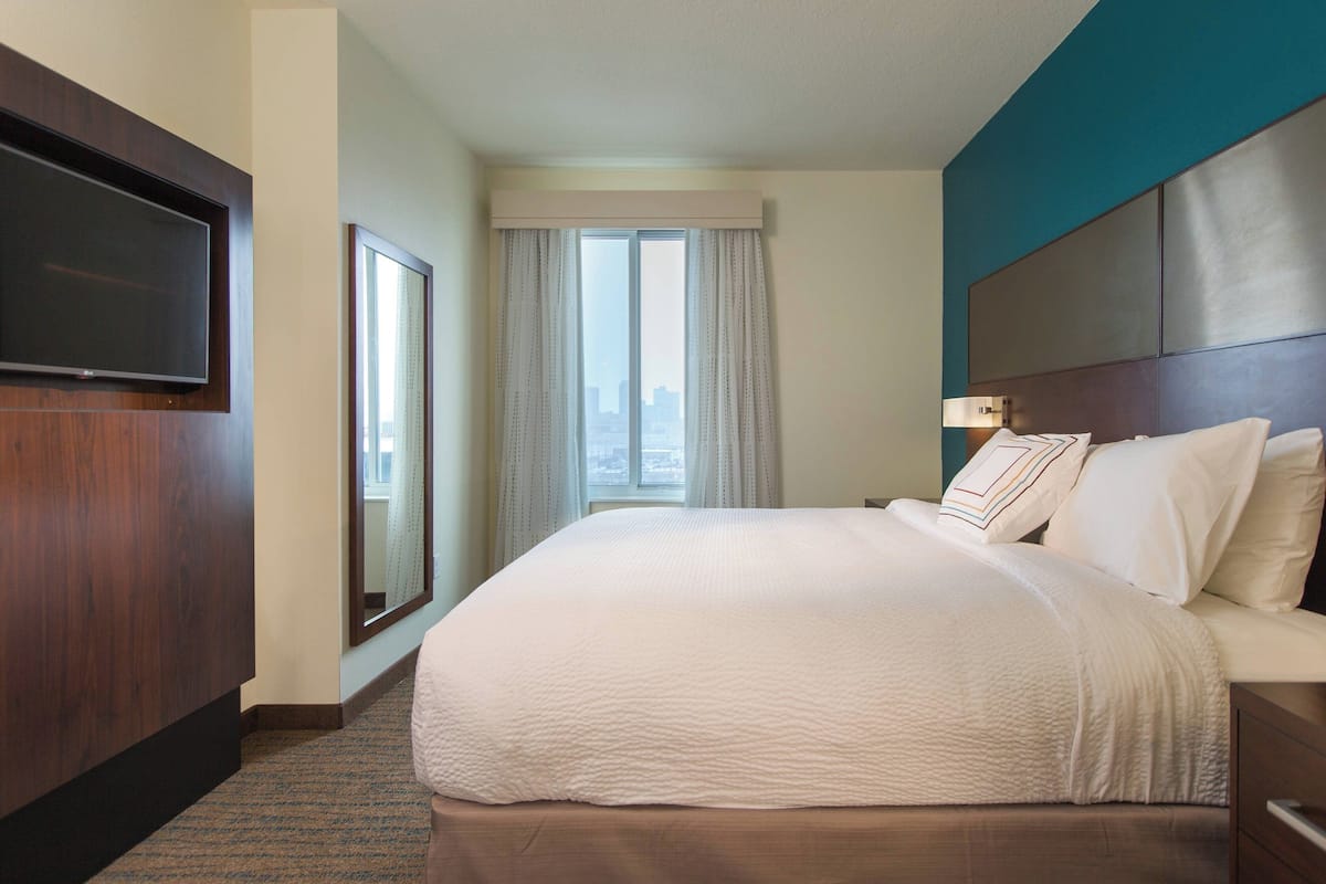 Une chambre d’hôtel avec un grand lit, un téléviseur à écran plat fixé au mur, une fenêtre avec des rideaux et une vue sur la ville.