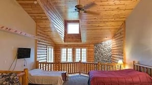 Camera in una baita di legno con due letti, una ventola a soffitto e una parete decorata in pietra.