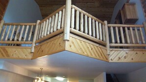 Un balcone in legno con ringhiera, un soffitto con travi a vista e un lampadario.