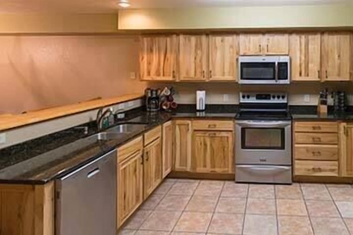 A kitchen with wooden cabinets, a stainless steel sink, a microwave, and an oven.
