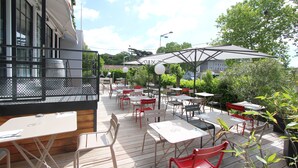 An outdoor patio with tables and chairs, some under umbrellas, and a building in the background. - Hotel Vol de Nuit (Toulouse)