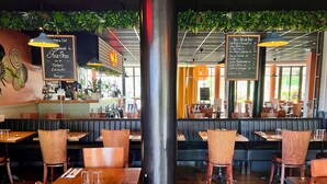 A restaurant interior with wooden tables and booths, a bar area, and hanging plants. - Hotel Vol de Nuit (Toulouse)