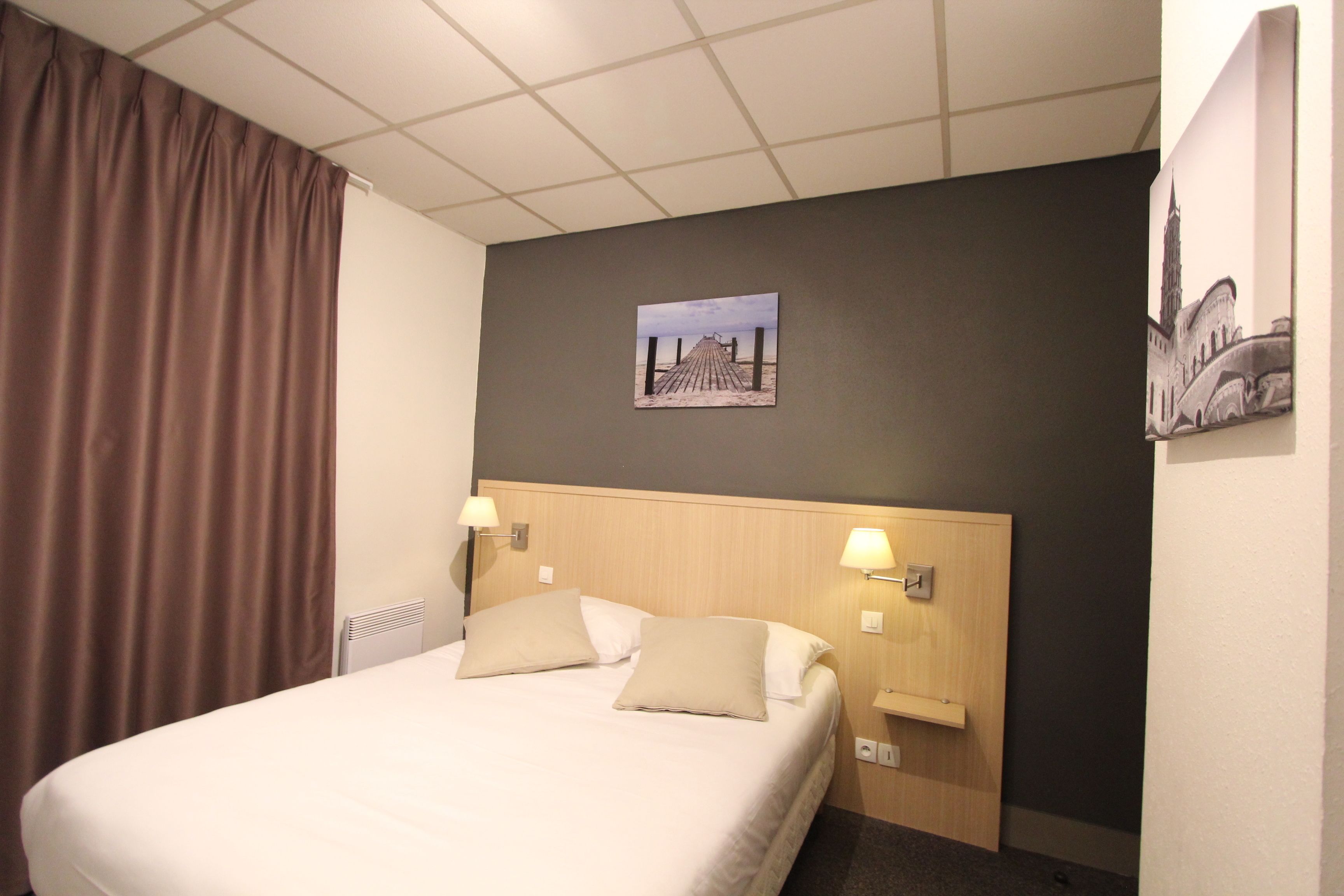 A hotel room with a large bed, two bedside lamps, a headboard, a wall-mounted picture, and a window with curtains.