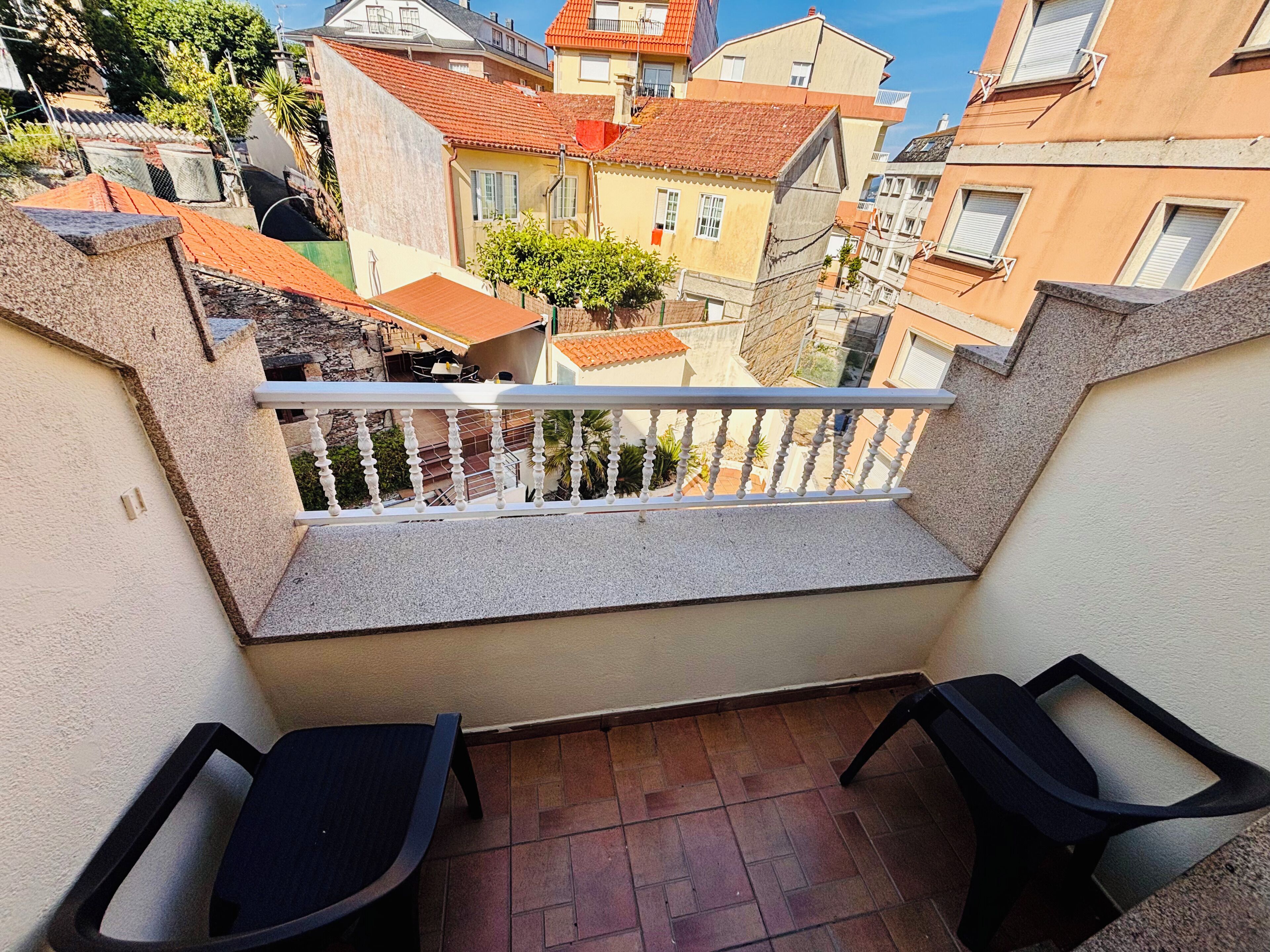 A balcony with two chairs, a view of neighboring buildings, and a tiled floor.