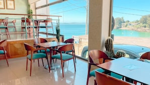A restaurant with a view of the sea, featuring wooden tables and chairs, a cactus plant, and framed pictures on the wall. - Hotel Atalaya II (Sanxenxo)