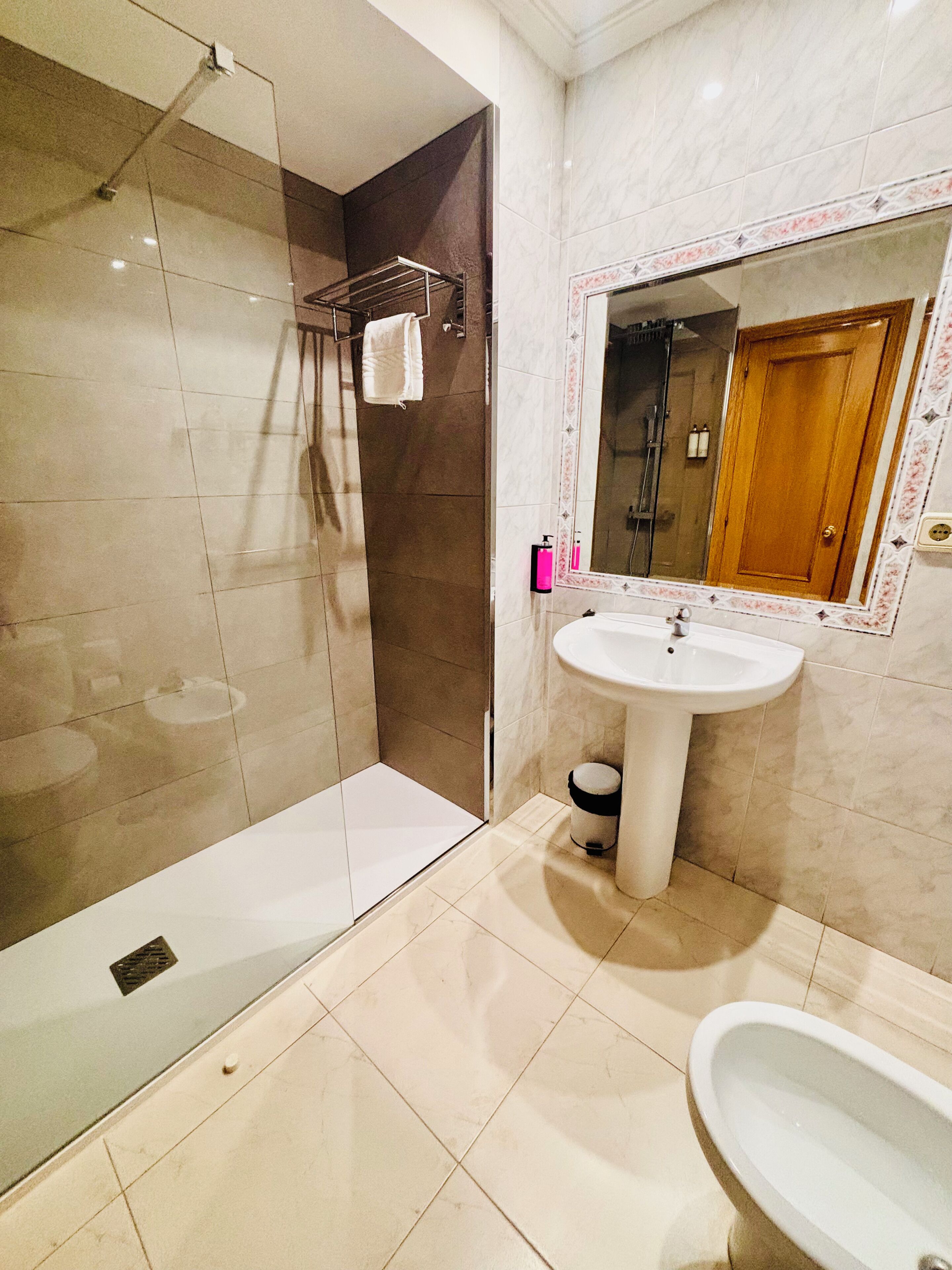 Een badkamer met een douchecabine van glas, een wastafel op een zuil en een bad.