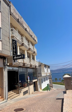 A hotel with a sign reading 'HOTEL ATALYA II,' a staircase leading to the entrance, and a view of the sea in the background. - Hotel Atalaya II (Sanxenxo)