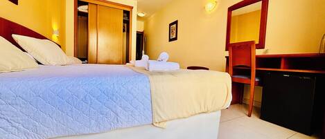 A hotel room with a bed, a desk, a chair, a wardrobe, and a television.